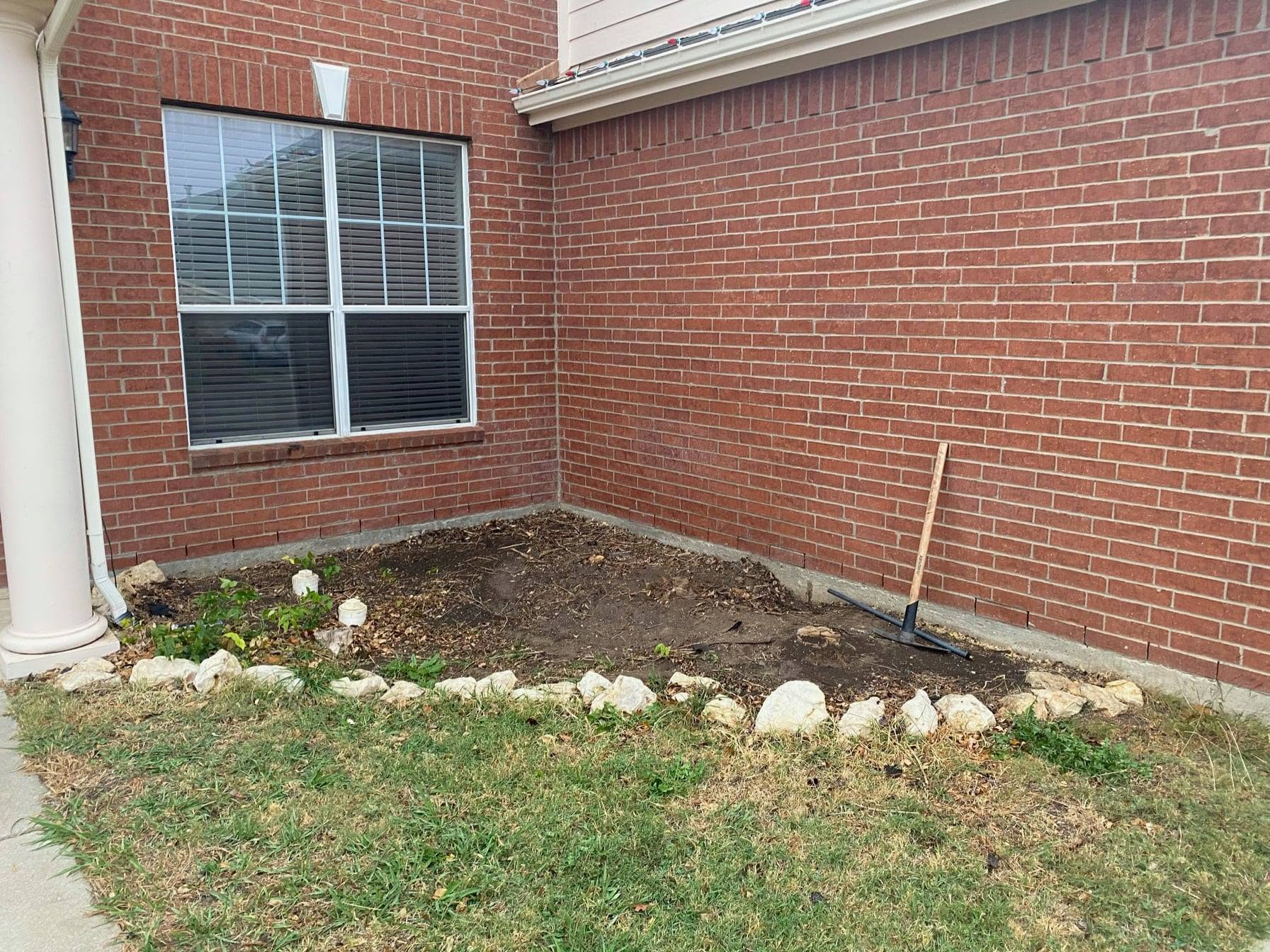Bare dirt bed against a brick home before landscaping