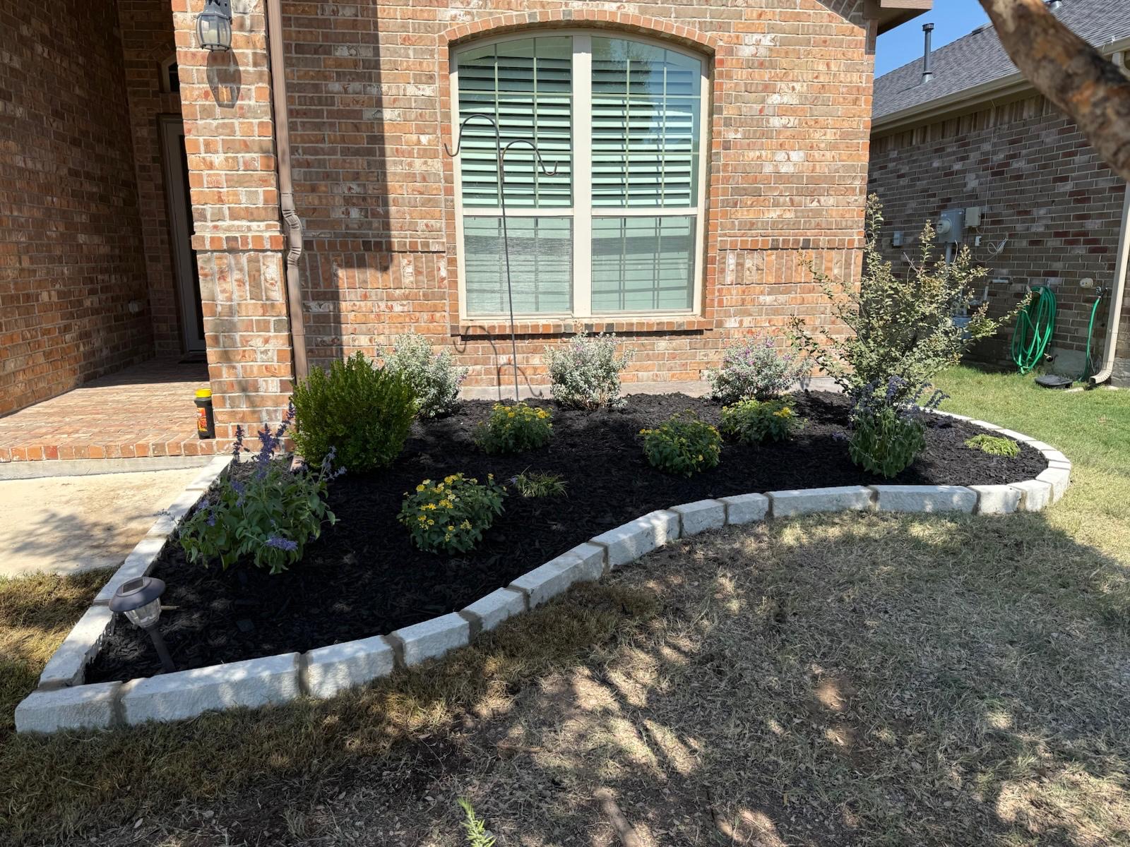 Finished residential flower bed with stone edging, fresh mulch and new plants