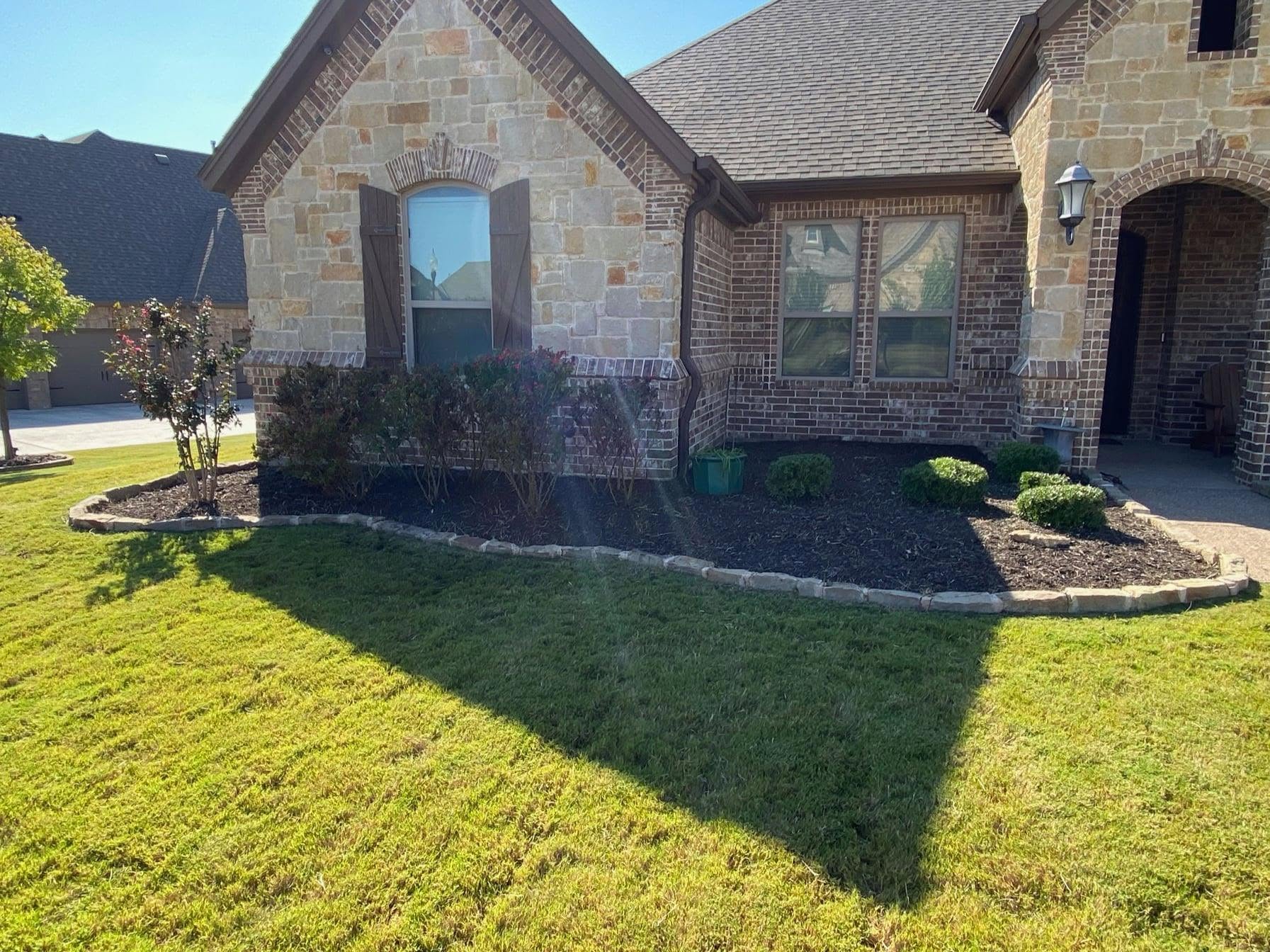Refreshed front beds and healthy lawn at a stone home