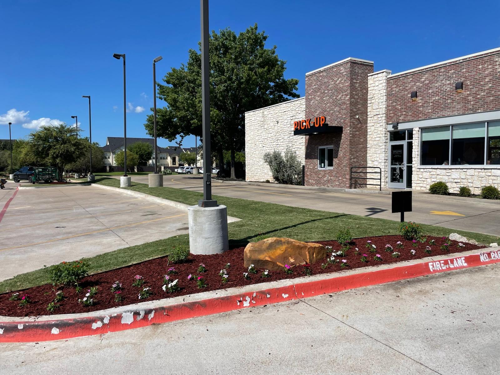 Landscaped pick-up area of a restaurant with trimmed beds and clean turf